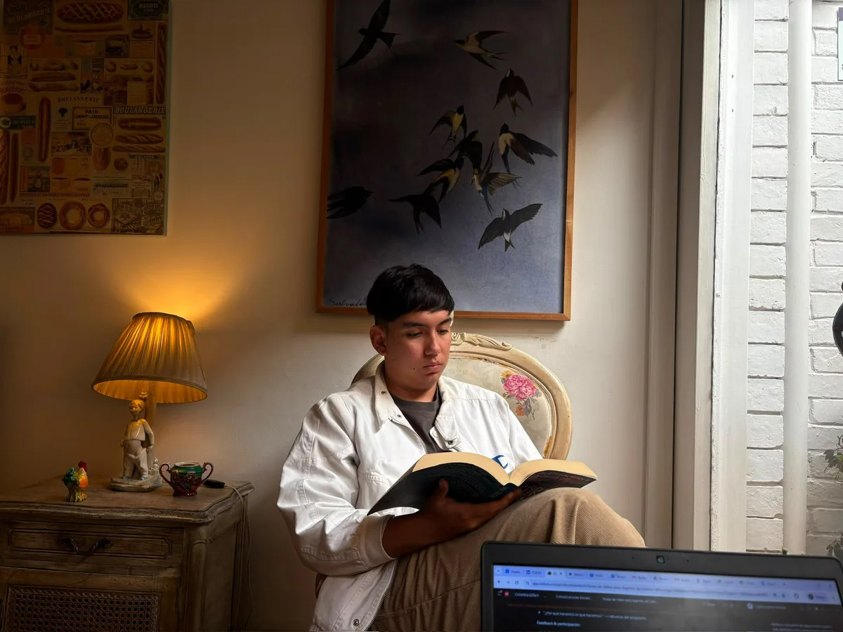 Kevin leyendo un libro en un sillón, junto a una lámpara encendida